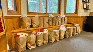 Bags of groceries are lined up in rows on top of and below a built in bench in a bay window.