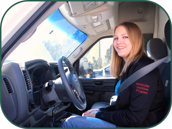 A young woman with long blonde hair and a black sweatshirt sits at the wheel of a vehicle.