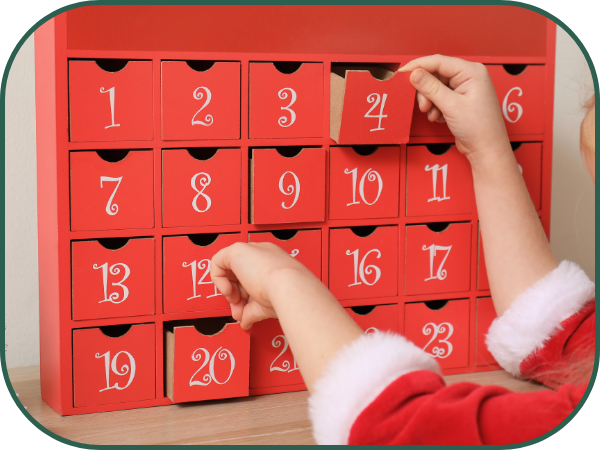 Two arms reach into the frame, garbed in red trimmed with white fur. They are opening drawers in a bright red Advent Calendar.