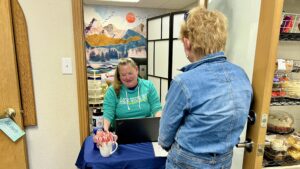 Volunteer Coordinator Kim sits at a table in the Food Share Market setting up an appointment for a client who is facing away from the camera.