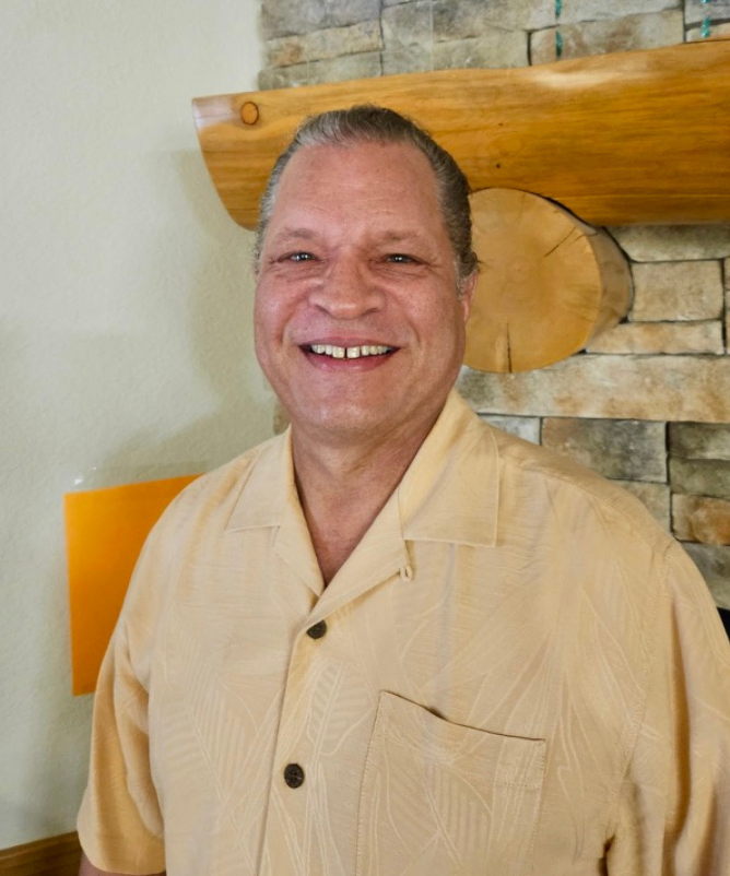 A smiling man with short dark hair and a yellow button-up shirt.